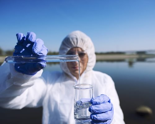Ecologist sampling water from the river with test tube.
