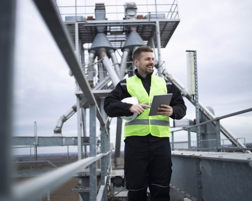 Industrial factory worker standing on high metal construction of production plant.