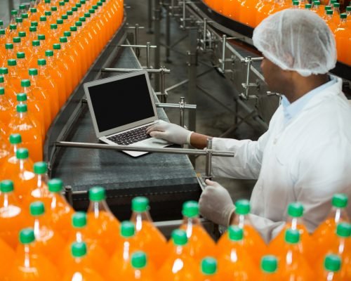 High angle view of male worker using laptop amidst production line in juice factory