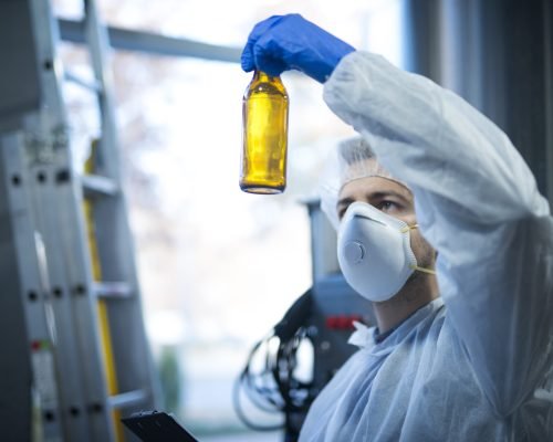 Technologist expert in beer production factory holding glass bottle and checking quality.